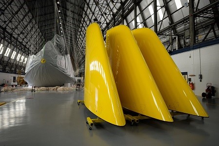 Giant tail fins await in the foreground as the envelope is installed over the framework of the newest Goodyear Blimp, being assembled this summer at Goodyear's Wingfoot Lake Hangar in Suffield, Ohio.   (PRNewsFoto/The Goodyear Tire & Rubber Company)