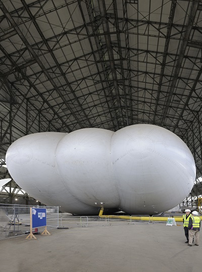 A yellow air duct keeps the Airlander 10 inflated for now, though helium will be pumped in later this year. The aft end, visible in this view, will house propulsors and tail units on the end of the outer lobes.  Credit: Mark Wagner, Aviation-Images.com 